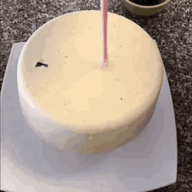 a white cake with pink frosting is sitting on a white plate on a counter .