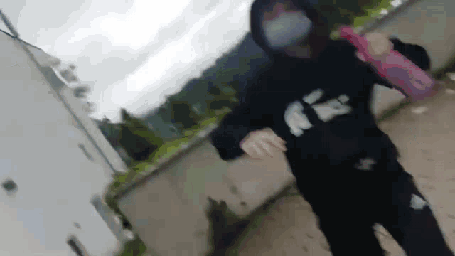 a person wearing a mask and a hoodie is walking down a sidewalk .