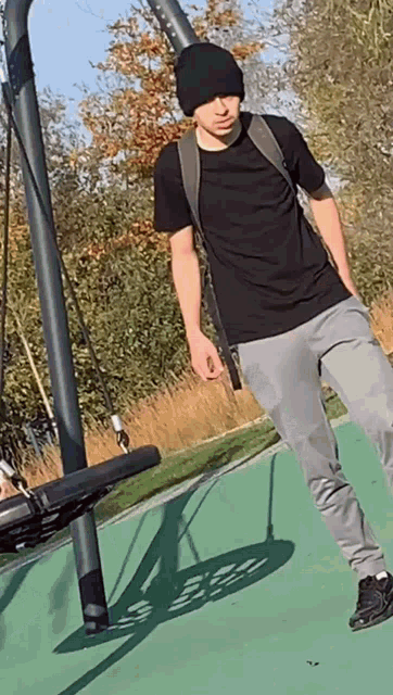 a young man wearing a black shirt and grey sweatpants is standing next to a swing
