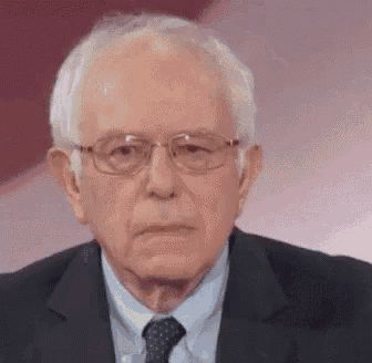 bernie sanders is wearing glasses and a suit and tie .