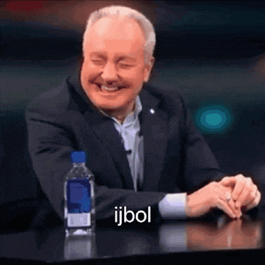 a man in a suit is sitting at a table with a bottle of water and the word ijbol on the table