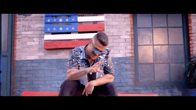a man wearing sunglasses is sitting on a red couch in front of an american flag