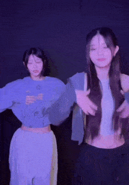 two girls are dancing in a dark room with purple lights behind them .