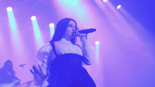 a woman singing into a microphone on a stage with purple lights behind her