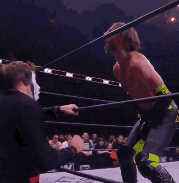a wrestler in a mask is holding a rope in front of a crowd that says aew