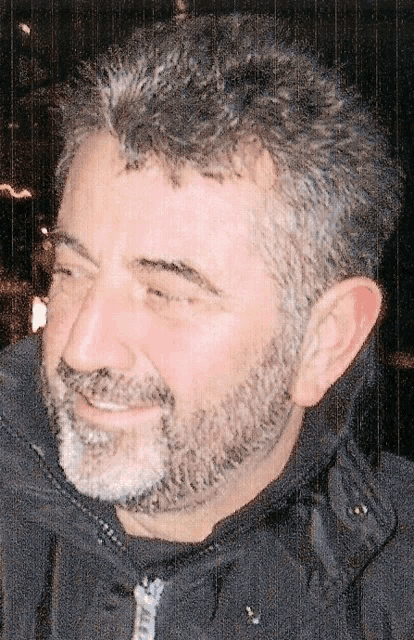 a man with a beard and a black jacket smiles for the camera
