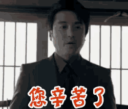 a man in a suit and tie is standing in front of a window with chinese writing on it .