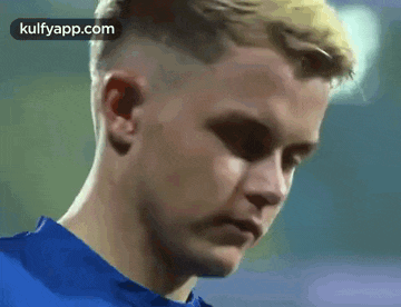 a young man in a blue shirt is looking at the camera with a serious look on his face .