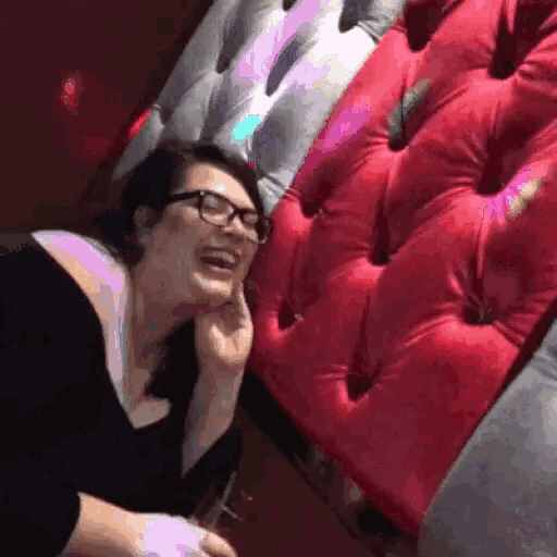 a woman wearing glasses is laughing in front of a red and gray couch .
