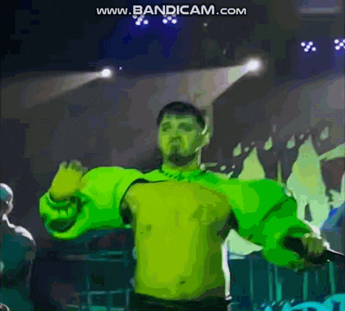 a shirtless man in a green jacket is dancing on a stage in front of a crowd .