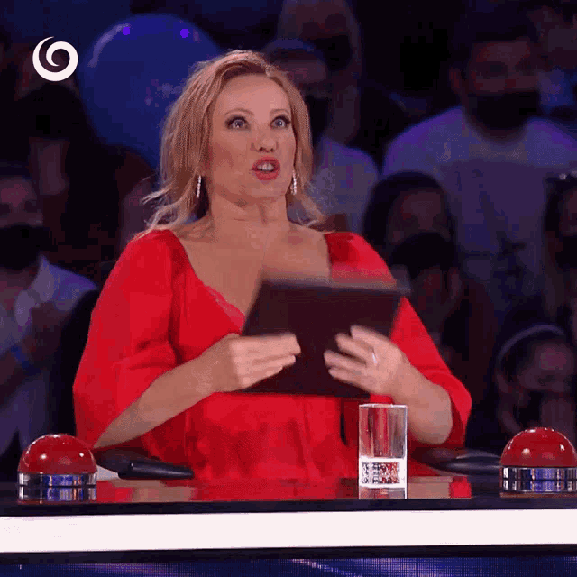 a woman in a red dress sits at a table holding a piece of paper