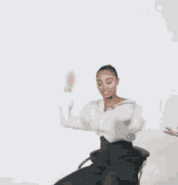 a woman in a white sweater and black pants is sitting in a chair with her arms outstretched .