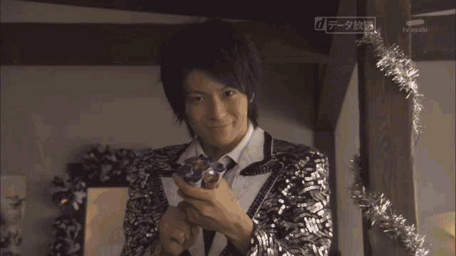 a man in a sequined suit is surrounded by tinsel and confetti and says tv asahi in the corner