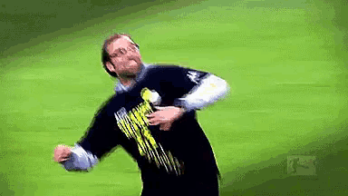 a man wearing a black shirt with a yellow logo on it is throwing a ball on a field