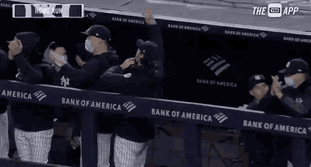 a group of baseball players standing in a dugout with a bank of america banner behind them