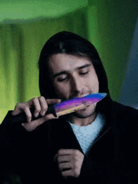 a man in a hooded jacket is holding a rainbow colored knife in his mouth .
