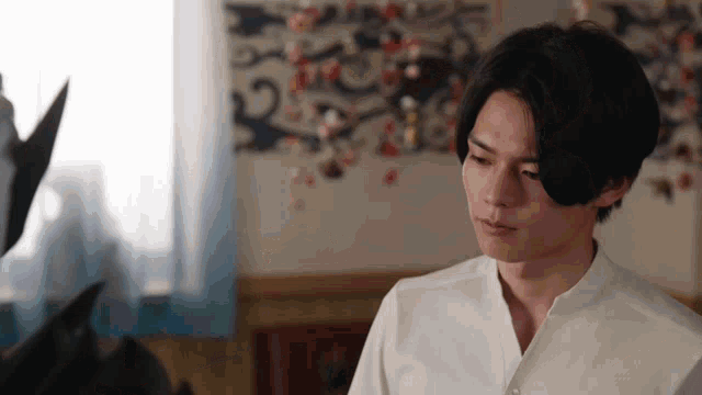 a young man in a white shirt is sitting in a room looking at something .