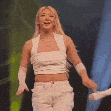 a woman in a white crop top and white pants is dancing on stage .