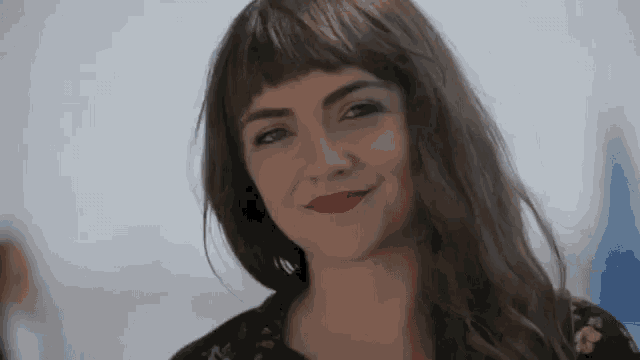 a woman with bangs and red lipstick is smiling for the camera .