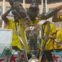 a man wearing a hat that says champions is pouring beer into a trophy