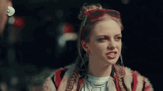 a woman wearing sunglasses and a braided ponytail looks to the side