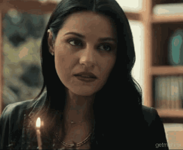 a woman is holding a candle in her hand and looking at the camera .