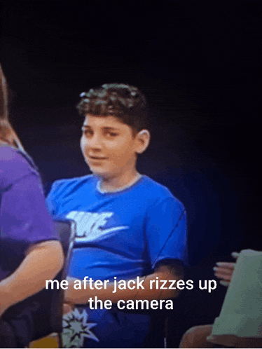 a boy in a blue nike shirt is sitting in a dark room