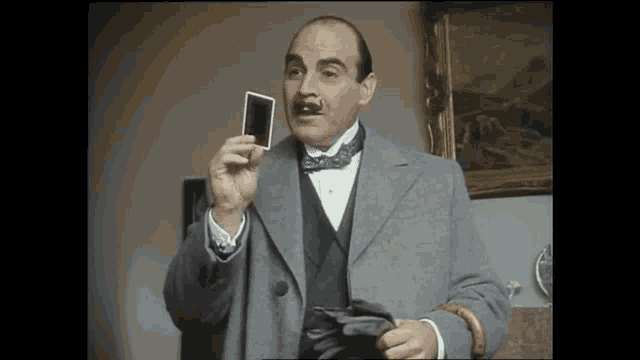 a man in a suit and bow tie is holding a playing card in his hand