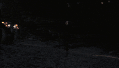 a man in a black hooded sweatshirt stands in front of a blurry background of lights