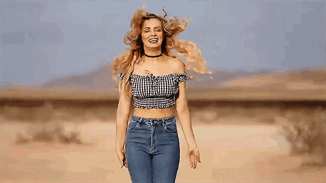 a woman in a crop top and jeans is walking through the desert .