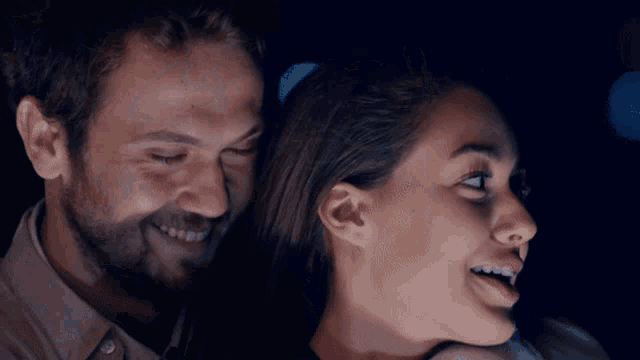 a man and a woman are smiling and looking at something in the dark