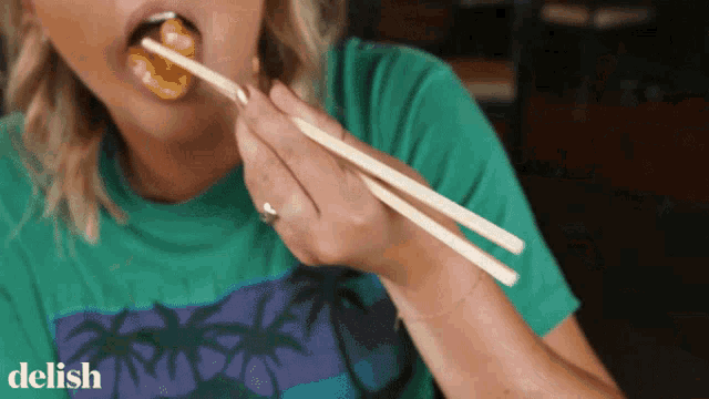 a woman in a green shirt is eating food with chopsticks