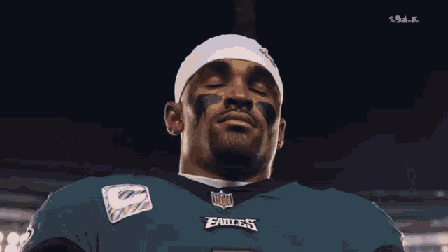 a man wearing a nfl eagles jersey looks down with his eyes closed