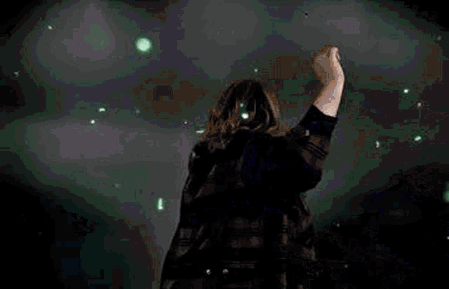 a woman in a plaid jacket is standing in a dark room with her arms outstretched in the air .