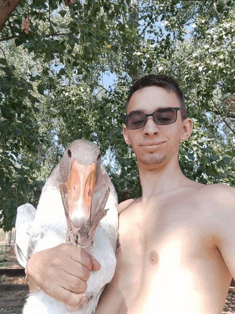 a shirtless man holding a large white goose