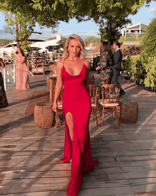 a woman in a red dress with a high slit is standing on a wooden deck