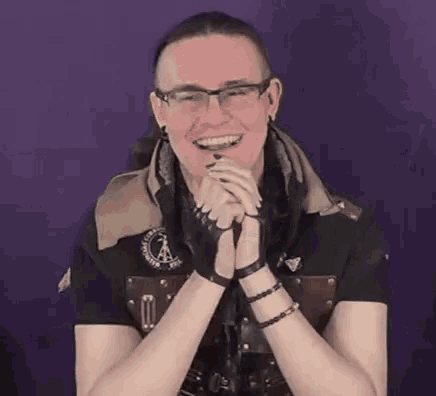 a man wearing glasses and a black shirt is smiling with his hands folded in front of him .