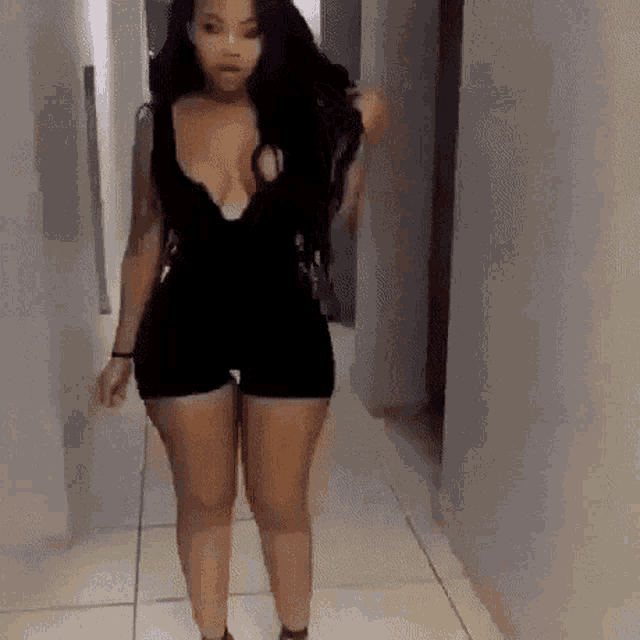 a woman is walking down a hallway wearing a black dress and shorts .