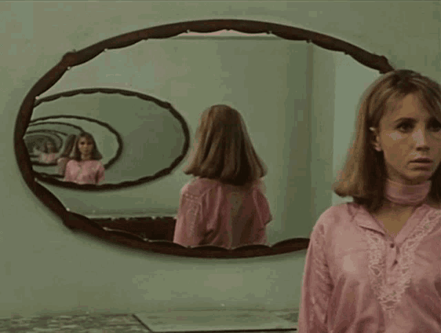 a woman in a pink shirt looks at her reflection in a mirror