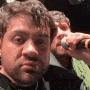 a man is singing into a microphone while another man looks on .