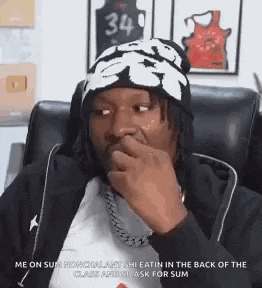 a man wearing a beanie is sitting in a chair covering his mouth .