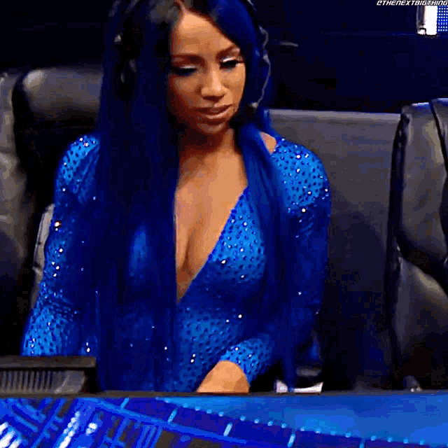 a woman with blue hair and headphones is sitting in front of a computer screen .