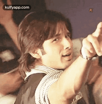 a man is pointing at the camera while wearing a watch .