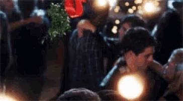 a couple kissing in a crowd with a mistletoe hanging from the ceiling
