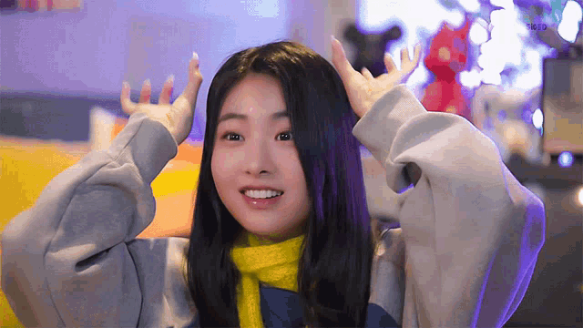 a girl wearing a grey sweatshirt and a yellow scarf is smiling