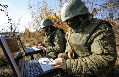 two soldiers are working on their laptops and one has a patch that says russia