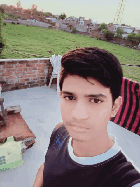 a young man taking a selfie in front of a field with a chair in the background