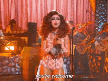 a woman singing into a microphone with the words " you 're welcome " behind her