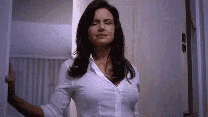 a woman in a white shirt is standing in front of a door with her eyes closed .