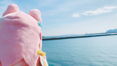a stuffed animal with pink hair and blue eyes is standing next to a body of water